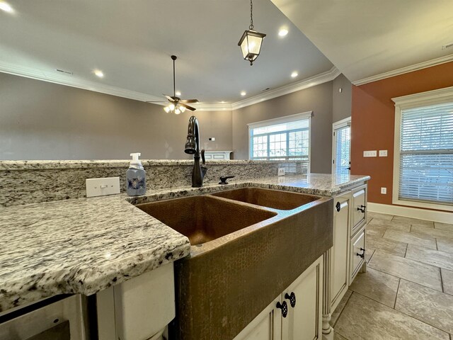 kitchen with light stone countertops, sink, ceiling fan, crown molding, and pendant lighting