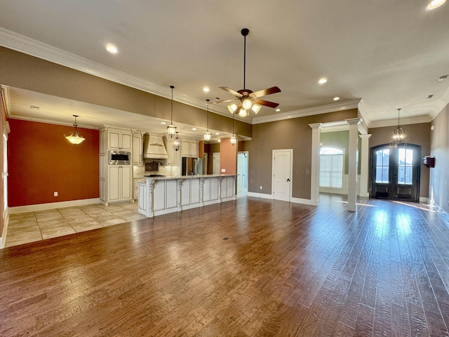 unfurnished living room with french doors, ornamental molding, ceiling fan with notable chandelier, and light wood-type flooring