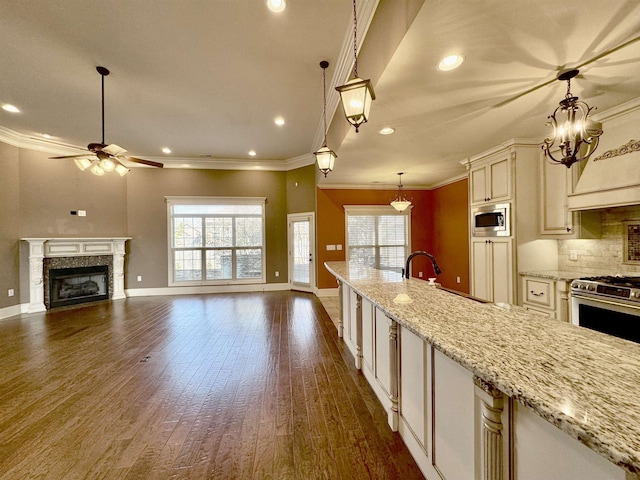 kitchen with hanging light fixtures, stainless steel appliances, light stone counters, ceiling fan with notable chandelier, and ornamental molding