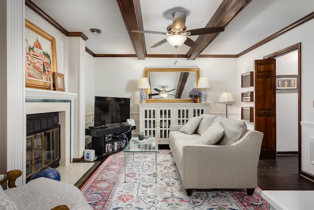 living room featuring ceiling fan, a fireplace, light hardwood / wood-style floors, beamed ceiling, and ornamental molding