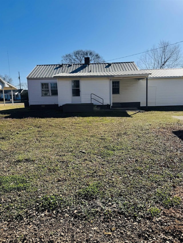 rear view of house featuring metal roof, a yard, and a chimney