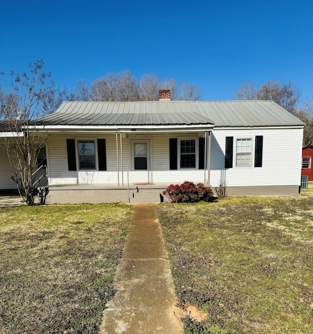 ranch-style house featuring metal roof, a front yard, a porch, and a chimney