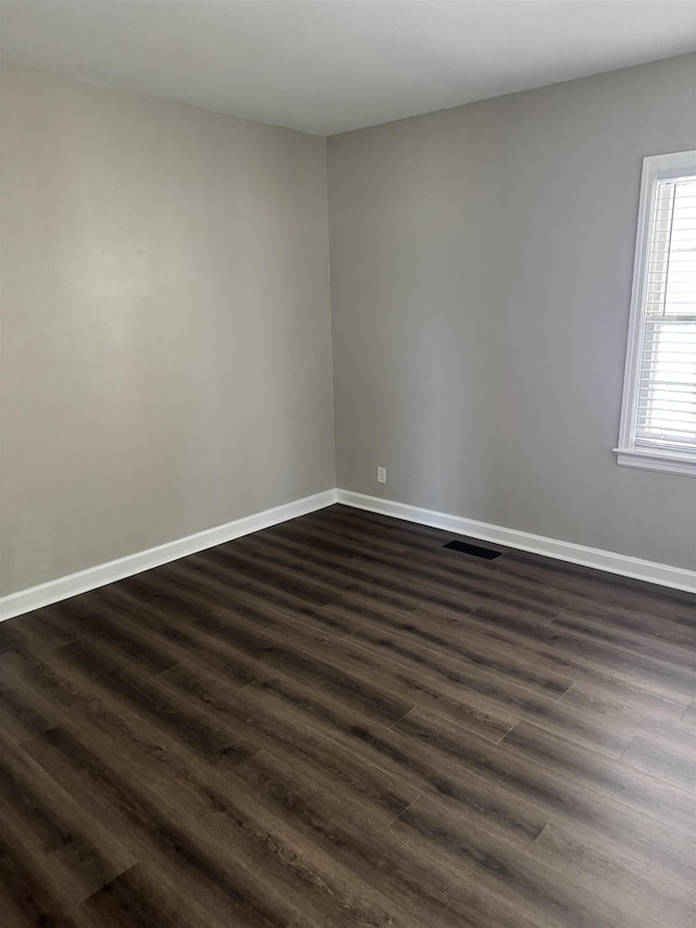 unfurnished room with visible vents, baseboards, and dark wood-style flooring