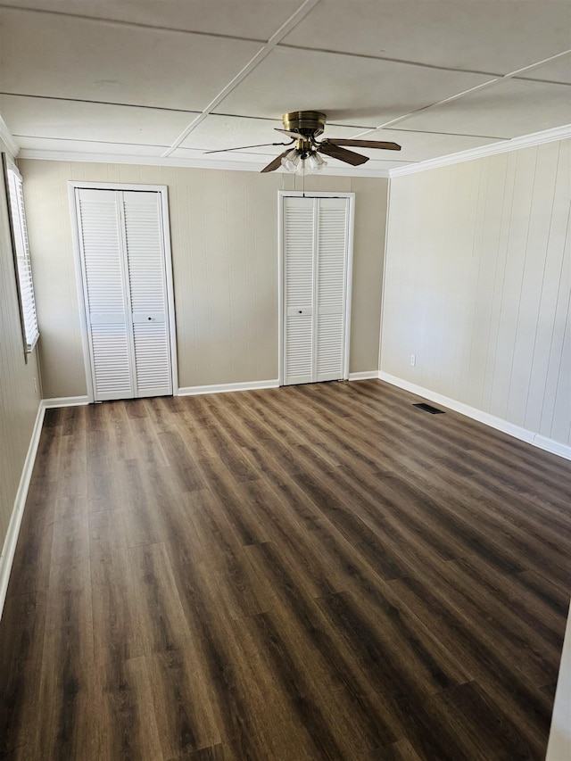 unfurnished bedroom with dark wood finished floors, baseboards, visible vents, and multiple closets