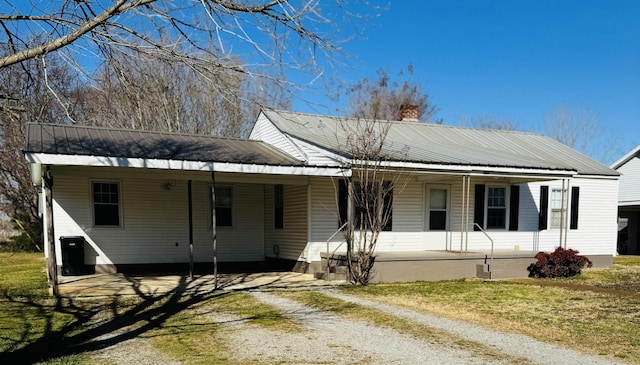 view of front facade with covered porch, a chimney, a carport, dirt driveway, and metal roof