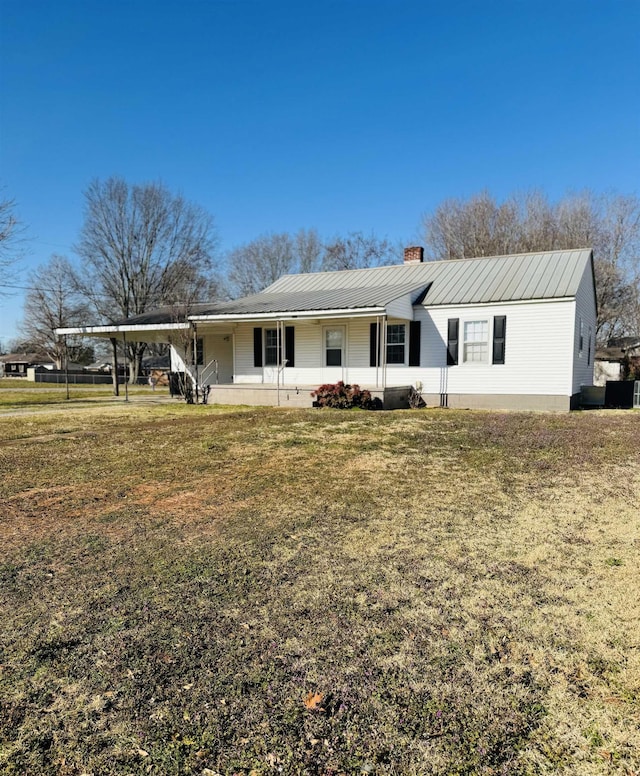 rear view of house featuring an attached carport, a porch, a chimney, a lawn, and metal roof