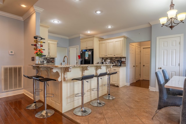  - kitchen featuring black fridge with ice dispenser, cream cabinetry, backsplash, light stone countertops, and crown molding