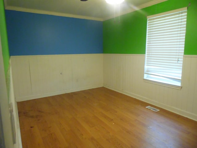  - unfurnished room featuring a wainscoted wall, wood finished floors, and crown molding