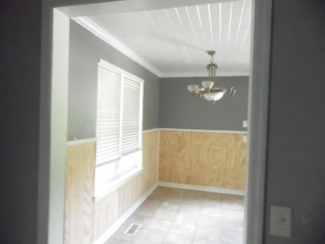 - unfurnished dining area with a chandelier, ornamental molding, a wainscoted wall, and wood walls