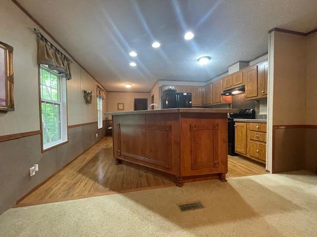 kitchen with lofted ceiling, light colored carpet, black appliances, and a kitchen island