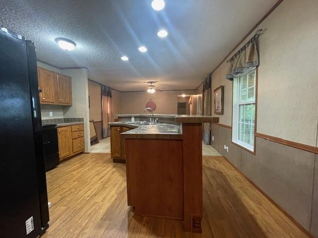 kitchen with sink, black refrigerator, light hardwood / wood-style floors, a textured ceiling, and a center island with sink