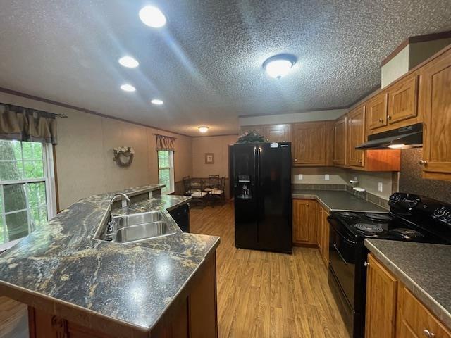 kitchen featuring sink, a large island with sink, black appliances, a textured ceiling, and light hardwood / wood-style flooring