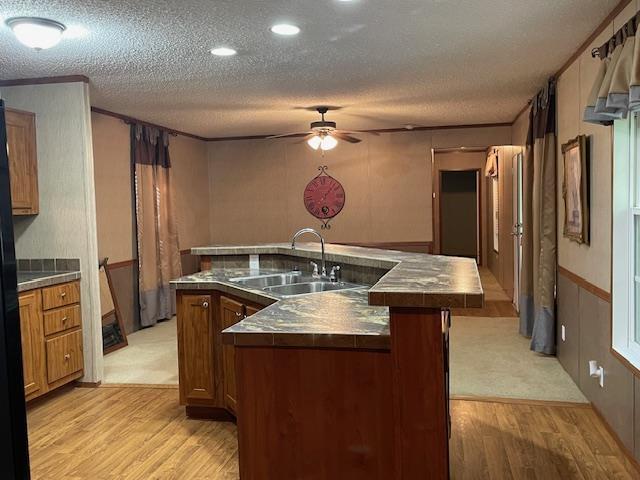 kitchen with a kitchen island with sink, sink, a textured ceiling, and light wood-type flooring