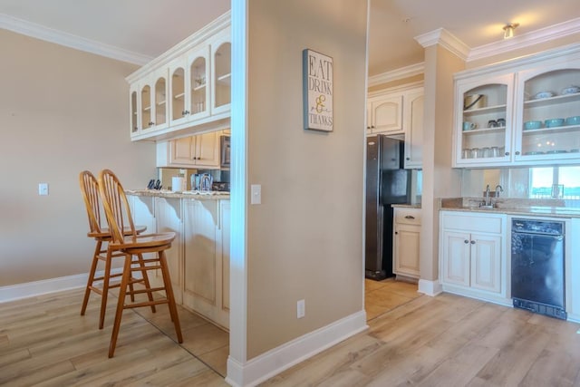 bar with black refrigerator, light stone countertops, crown molding, sink, and light hardwood / wood-style floors