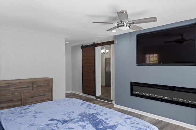 bedroom featuring a barn door, baseboards, a ceiling fan, and wood finished floors