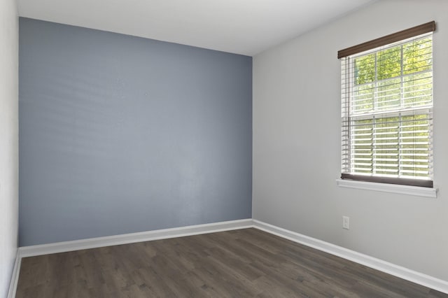 empty room featuring a wealth of natural light, dark wood-type flooring, and baseboards