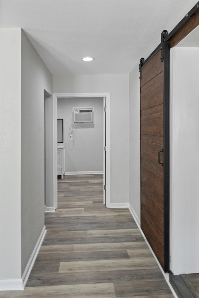 hallway featuring a barn door, wood finished floors, a wall mounted AC, baseboards, and recessed lighting