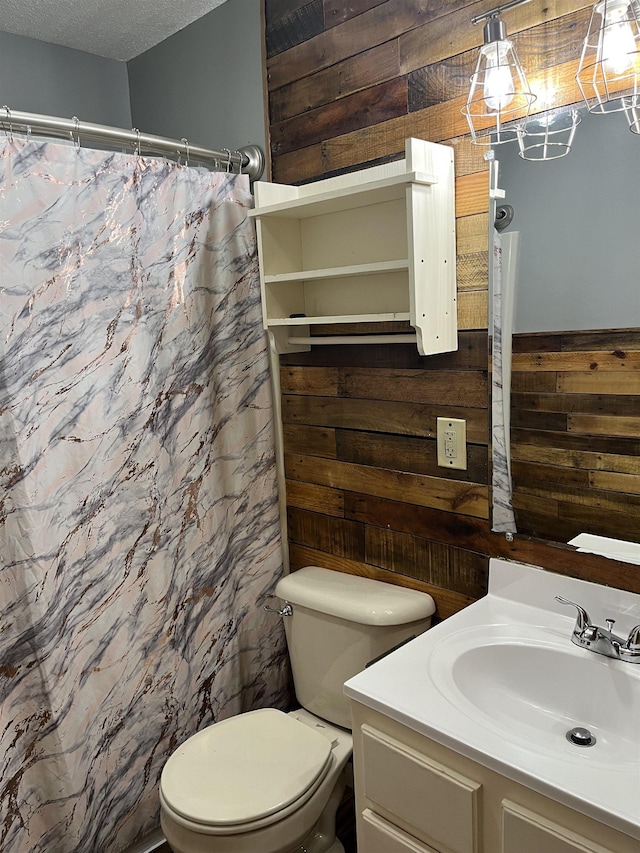bathroom with a textured ceiling, wood walls, toilet, and vanity