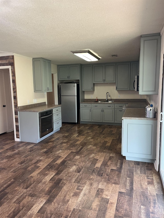 kitchen featuring a sink, a textured ceiling, stainless steel appliances, visible vents, and dark wood-type flooring