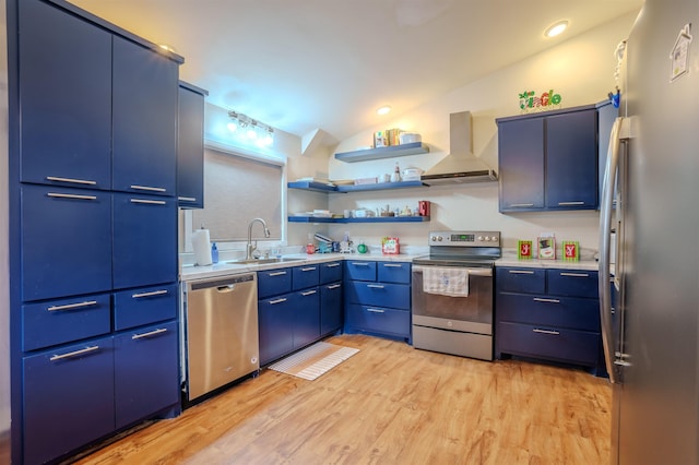 kitchen with stainless steel appliances, vaulted ceiling, a sink, wall chimney range hood, and light wood-type flooring