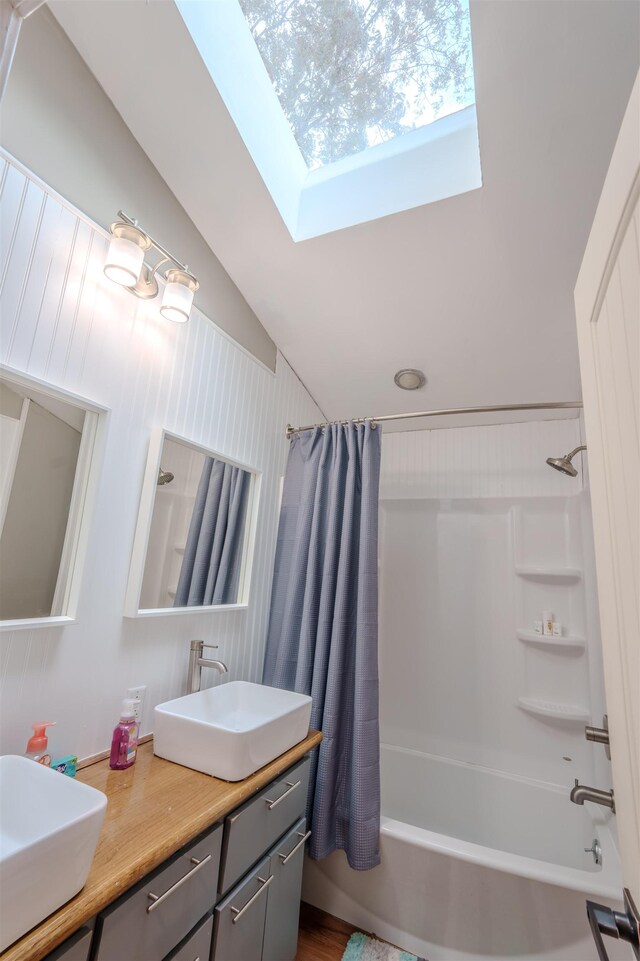 full bath featuring double vanity, shower / tub combo, vaulted ceiling with skylight, and a sink