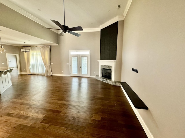 unfurnished living room featuring dark wood-type flooring, french doors, ceiling fan with notable chandelier, ornamental molding, and a fireplace