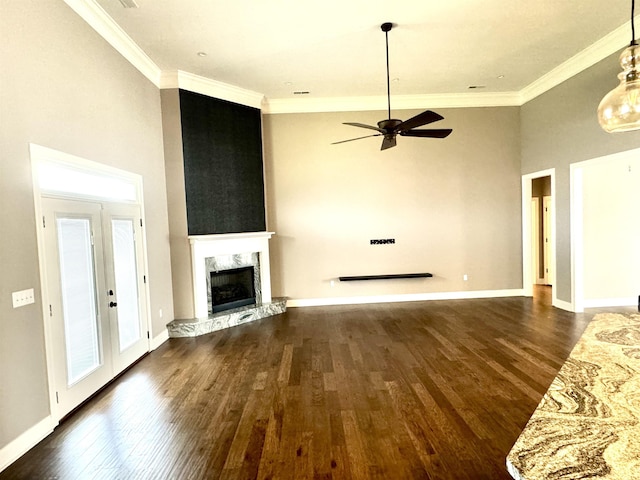 unfurnished living room featuring french doors, dark hardwood / wood-style flooring, ornamental molding, ceiling fan, and a stone fireplace