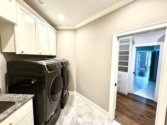 laundry room featuring washing machine and dryer, light hardwood / wood-style floors, cabinets, and ornamental molding