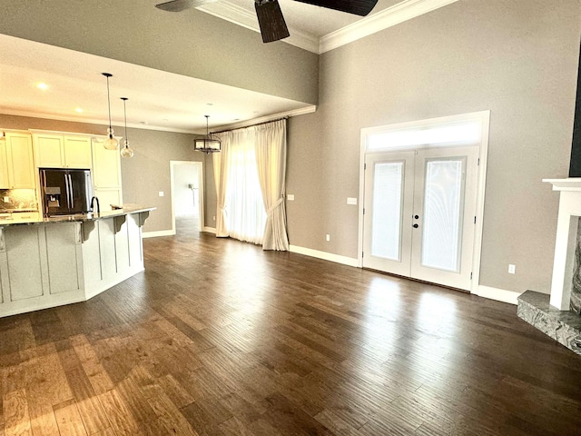 unfurnished living room featuring ceiling fan, a stone fireplace, ornamental molding, and dark wood-type flooring