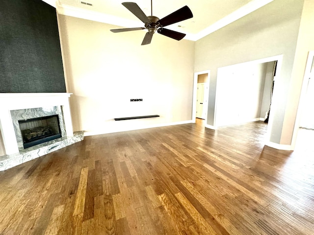 unfurnished living room featuring a towering ceiling, a premium fireplace, hardwood / wood-style floors, and ceiling fan