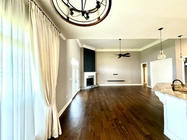 unfurnished living room with dark hardwood / wood-style flooring, sink, ceiling fan with notable chandelier, and ornamental molding