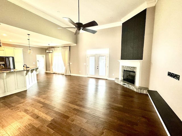 unfurnished living room featuring ceiling fan with notable chandelier, dark wood-type flooring, crown molding, sink, and a fireplace