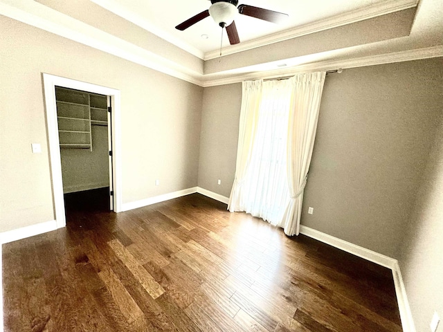 unfurnished bedroom with a raised ceiling, a walk in closet, ceiling fan, dark hardwood / wood-style floors, and a closet