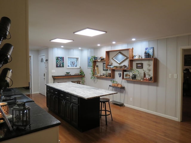 kitchen with a kitchen breakfast bar, dark brown cabinetry, a center island, and hardwood / wood-style floors