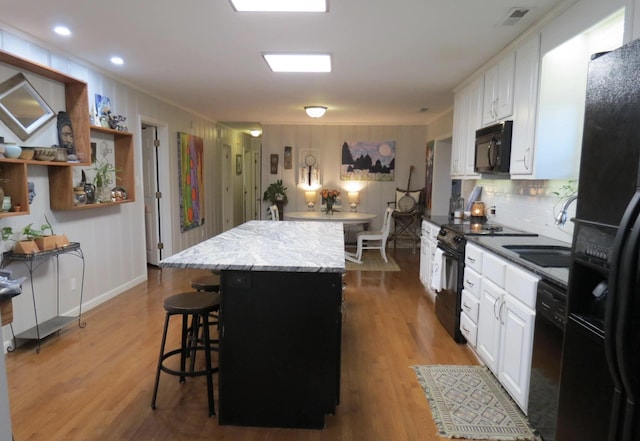 kitchen with black appliances, a center island, white cabinetry, and hardwood / wood-style floors