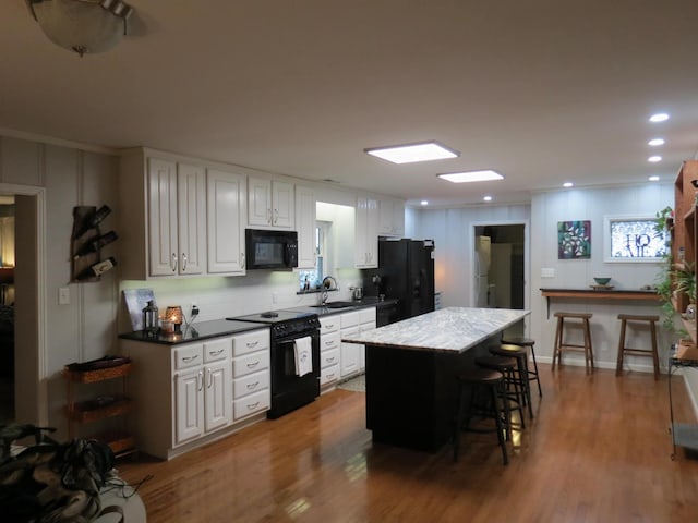 kitchen with a kitchen bar, white cabinetry, a kitchen island, and black appliances