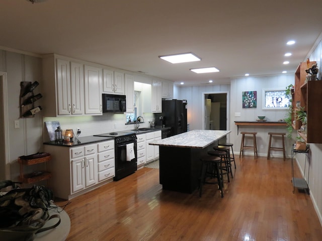 kitchen featuring a center island, a kitchen bar, white cabinets, black appliances, and hardwood / wood-style flooring