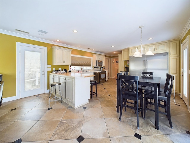 kitchen featuring a kitchen bar, cream cabinets, decorative light fixtures, and crown molding