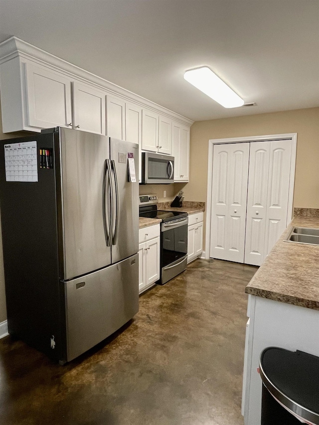 kitchen featuring stainless steel appliances, a sink, finished concrete floors, and white cabinets