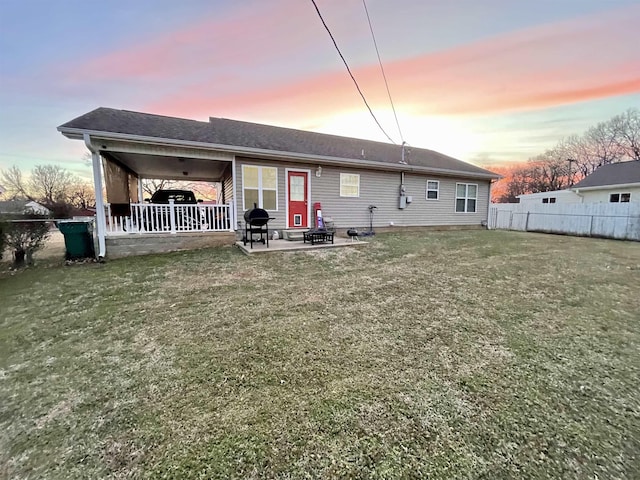 back of house at dusk with a patio area, fence, and a lawn