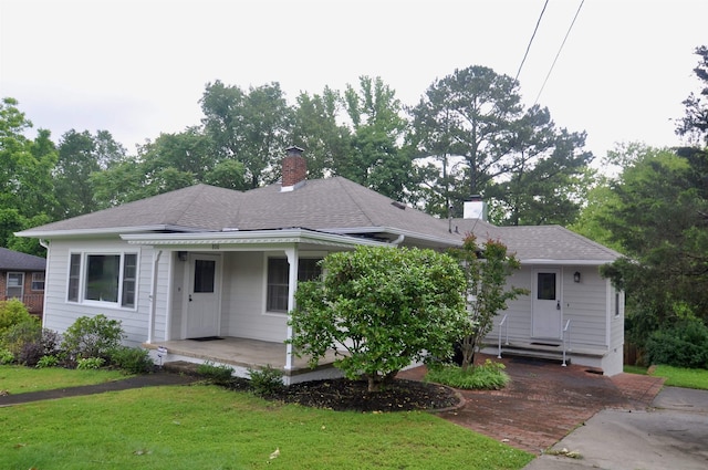  - view of front facade featuring a porch, a front yard, a chimney, and a shingled roof
