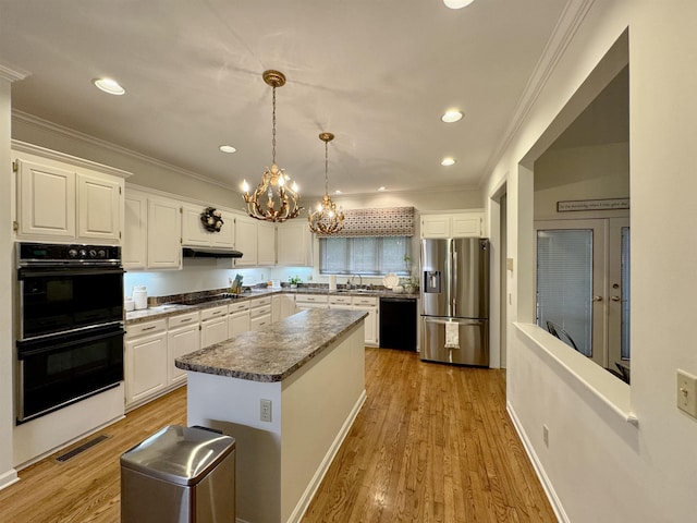 kitchen with a center island, black appliances, sink, decorative light fixtures, and white cabinetry