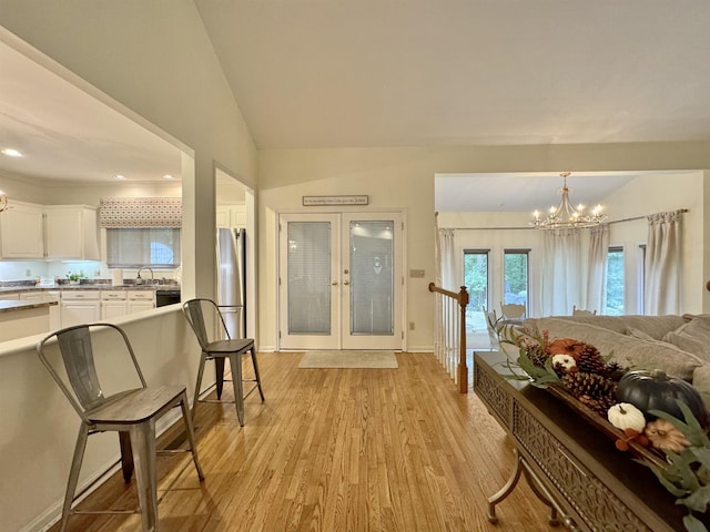 interior space with a chandelier, french doors, light wood-type flooring, and lofted ceiling