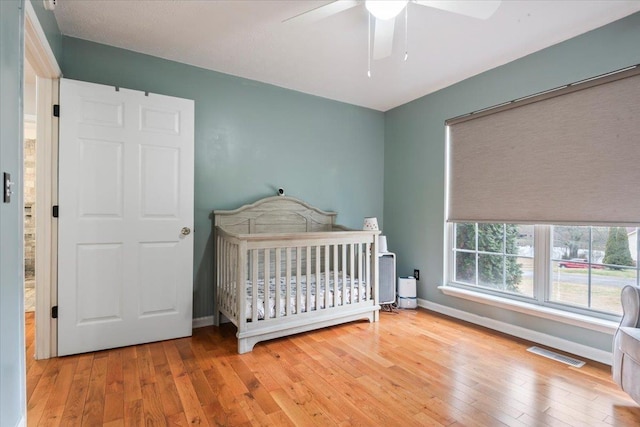 bedroom featuring ceiling fan, light hardwood / wood-style floors, and a crib