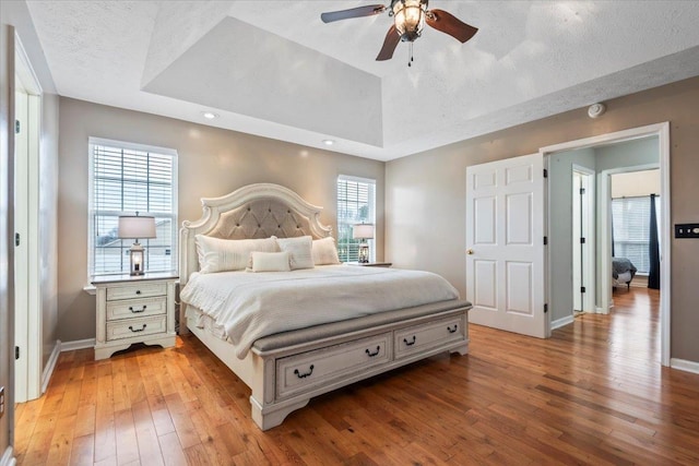 bedroom featuring lofted ceiling, a tray ceiling, light hardwood / wood-style floors, and a textured ceiling