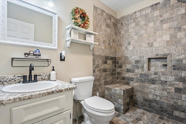 bathroom with vanity, a textured ceiling, toilet, and tiled shower