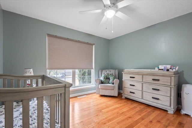 bedroom with ceiling fan, a crib, and light wood-type flooring