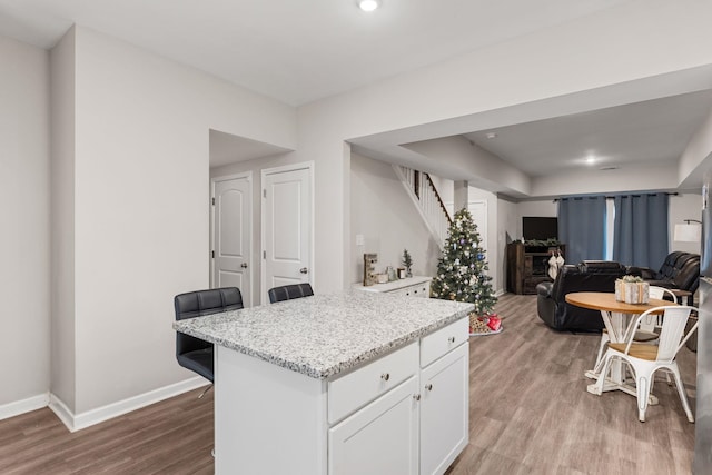 kitchen with light stone counters, a breakfast bar, white cabinets, and light wood-type flooring