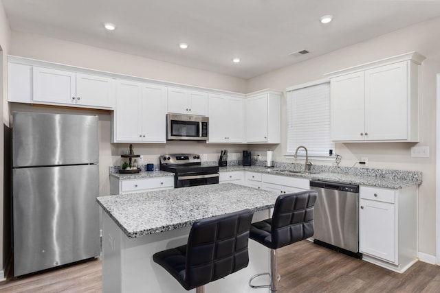 kitchen with white cabinetry, sink, a kitchen bar, a kitchen island, and appliances with stainless steel finishes