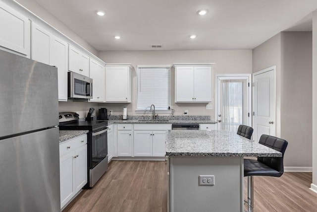 kitchen featuring light stone countertops, sink, a center island, a kitchen breakfast bar, and appliances with stainless steel finishes